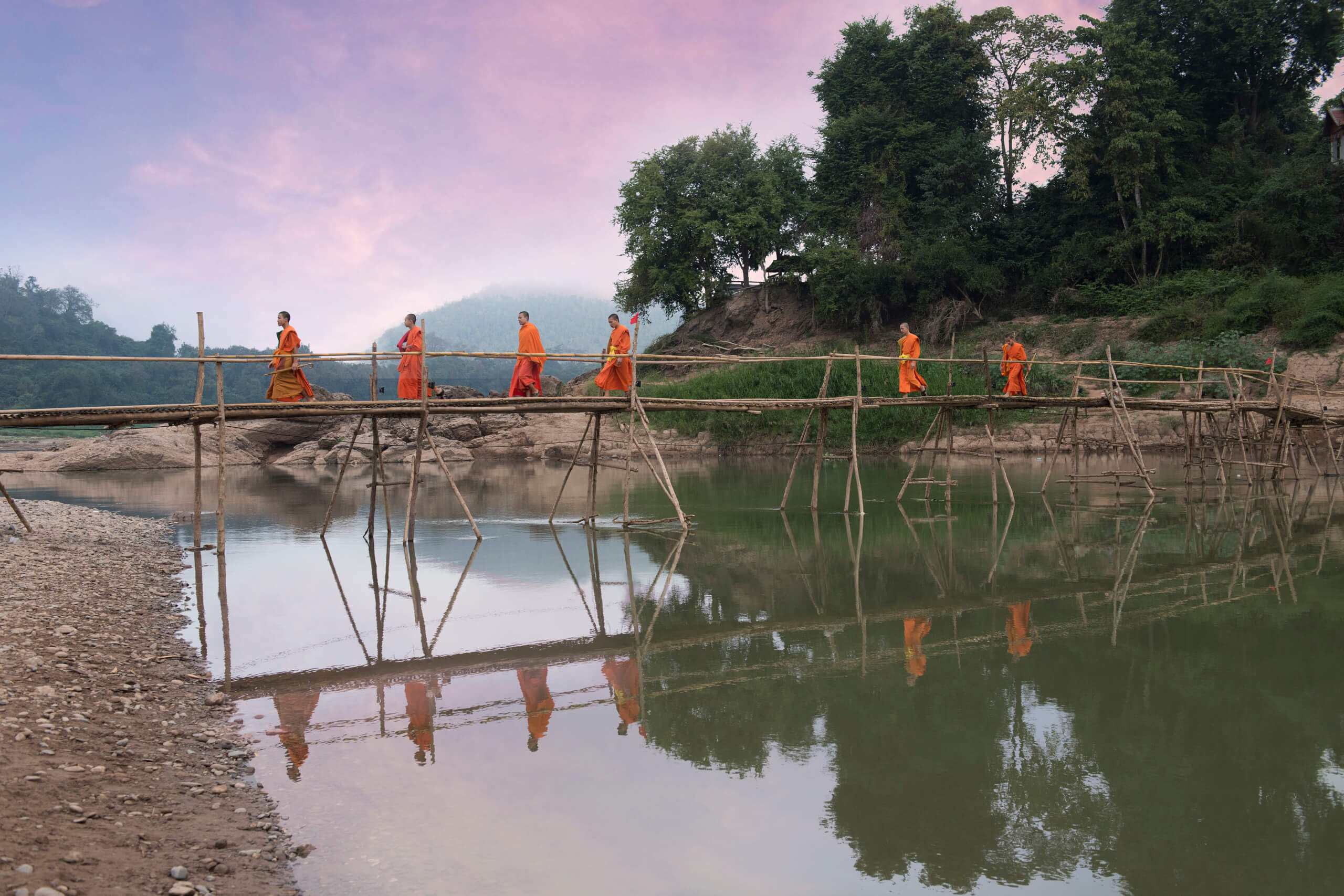 Monks crossing river on bamboo bridge